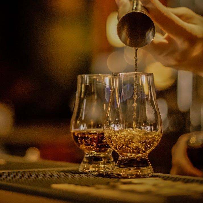 Bartender pouring whisky into two dram glasses with a blurred background