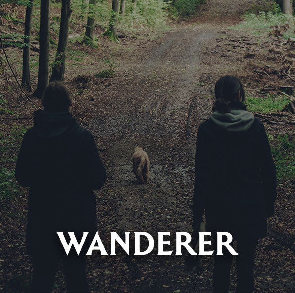Two people walking a dog on a path through a forest with 'Wanderer' text overlay.